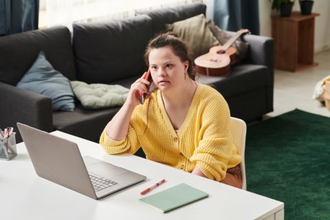 Person sitting at a desk in front of computer talking on a mobile phone