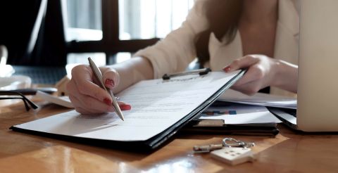 real estate agent assisting client to sign contract paper at desk with house model