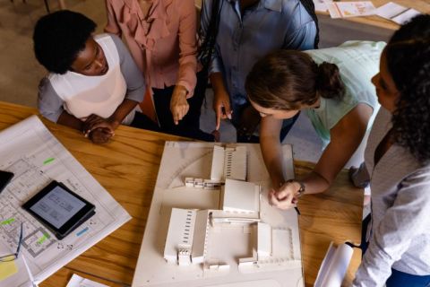 Diverse female architects in discussion using model and blueprints in casual office meeting