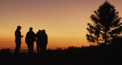 The silhouette of four people talking together in front of an orange sunset.